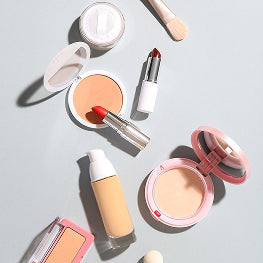 Makeup products including a compact, lipstick, and foundation on a light gray background